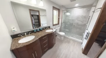 Modern bathroom remodel by Stately Kitchen and Bath in Gettzville, NY, featuring a double vanity with granite countertops, large mirror, and a spacious glass-enclosed shower.