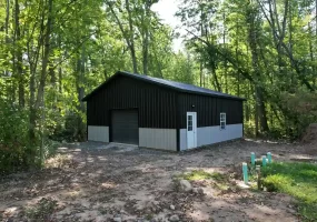 Front and side view of a modern black and gray pole barn in Clarence, NY, featuring durable metal siding and a custom garage door.