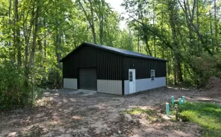 Front and side view of a modern black and gray pole barn in Clarence, NY, featuring durable metal siding and a custom garage door.