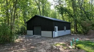 Front and side view of a modern black and gray pole barn in Clarence, NY, featuring durable metal siding and a custom garage door.