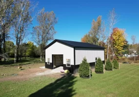 Side view of Stately Pole Barn with black wainscot, surrounded by greenery and trees.