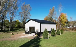 Side view of Stately Pole Barn with black wainscot, surrounded by greenery and trees.