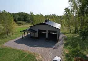 Aerial view of a finished Stately Pole Barn with black roofing, two cupolas, and surrounding green landscape.