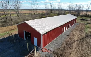 Side angle of the agricultural pole barn, featuring multiple white panel doors and clean, gravel-lined perimeter.