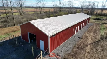 Side angle of the agricultural pole barn, featuring multiple white panel doors and clean, gravel-lined perimeter.